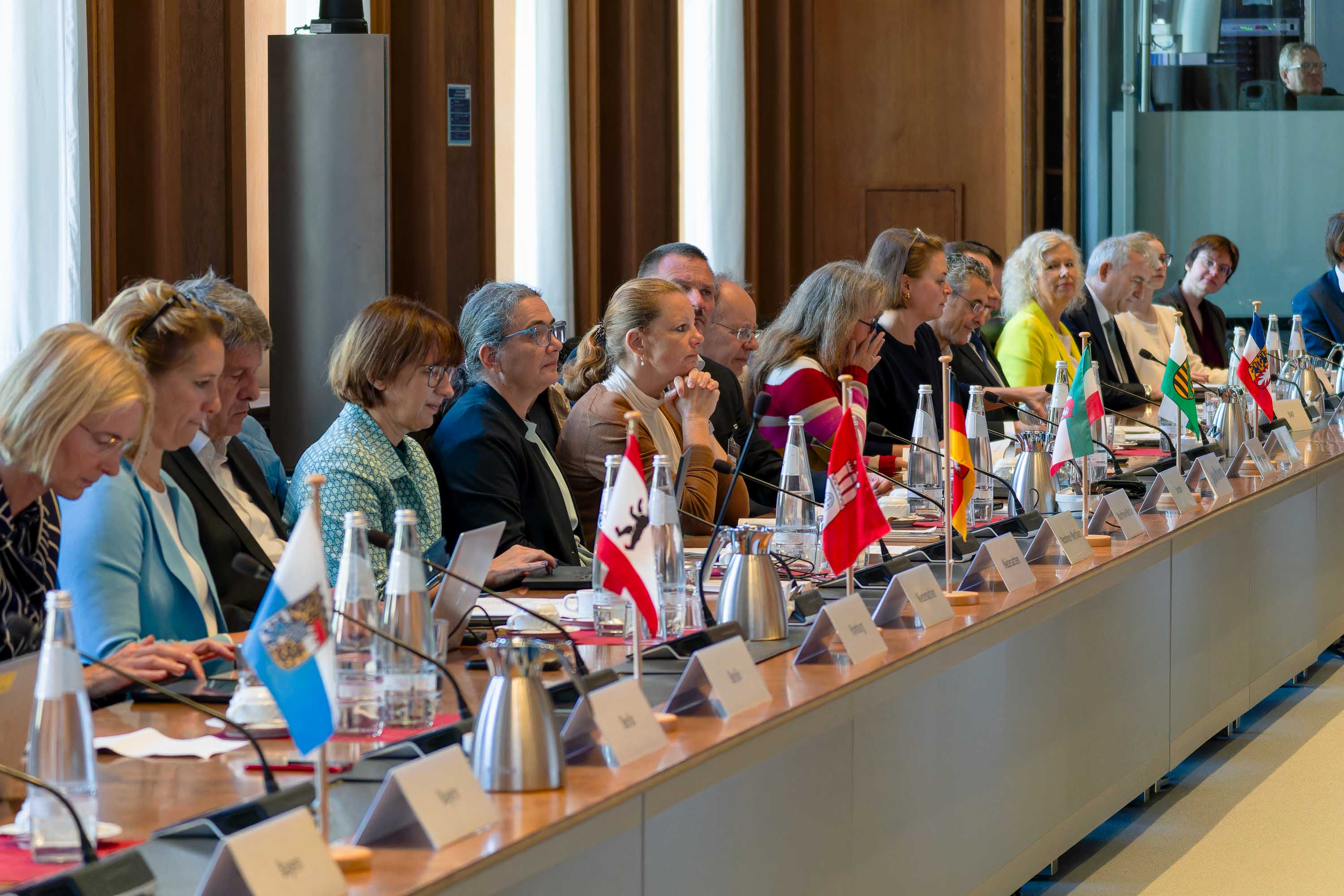 Anwesende des Bund-Länder-Treffen im BMF sitzen nebeneinander an einem lange Tisch - vor ihnen sind kleine Länderflaggen aufgestellt.